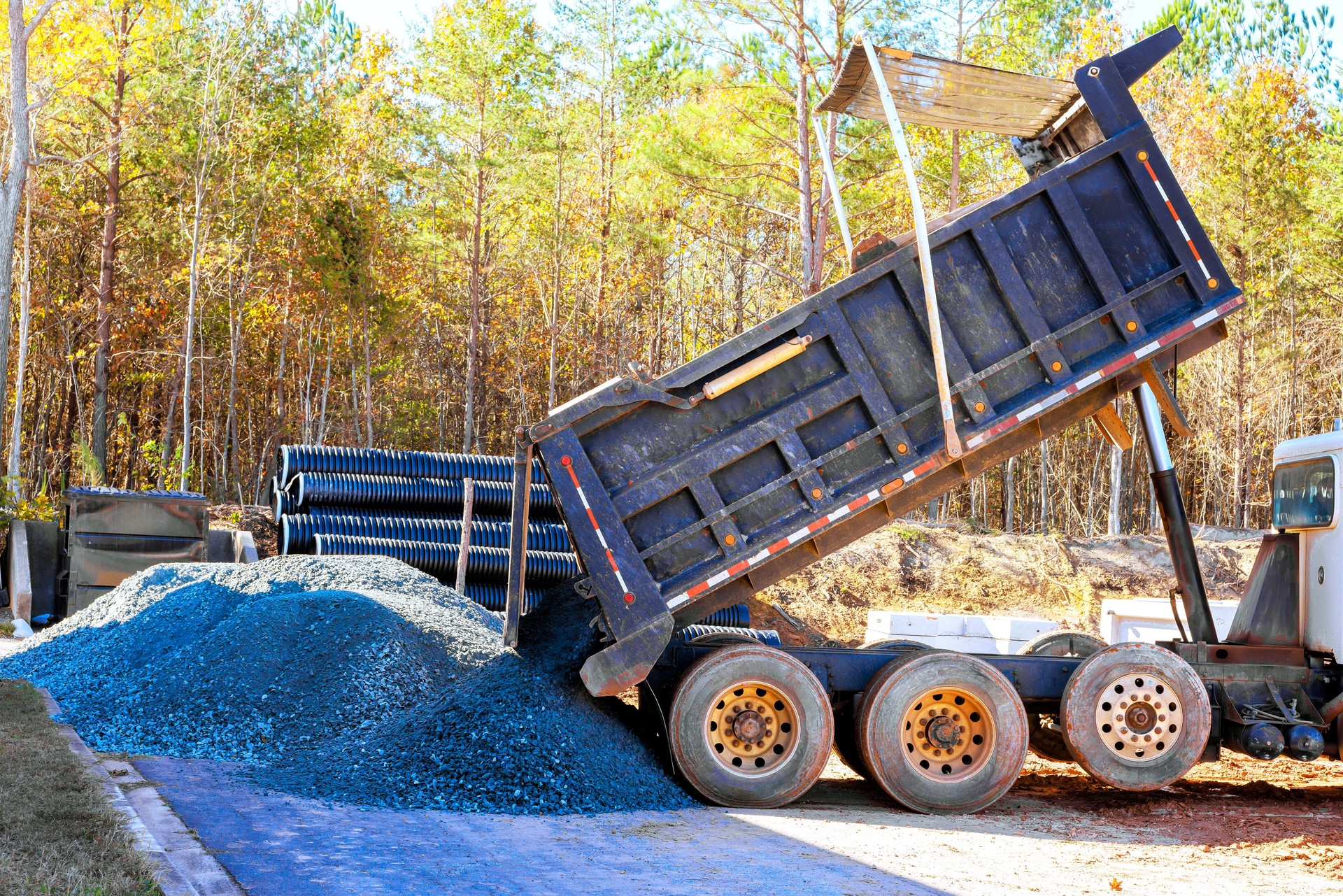 Dump truck unloading gravel at a construction site surrounded by trees during daytime