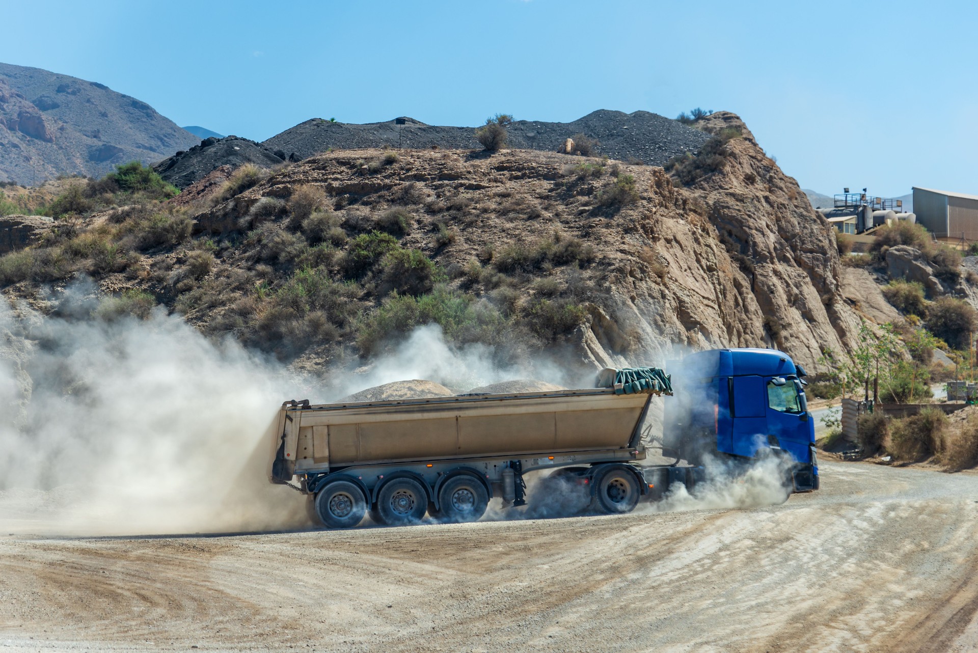 Truck with a dump semi-trailer for earthmoving, loaded and raising a large cloud of dust.